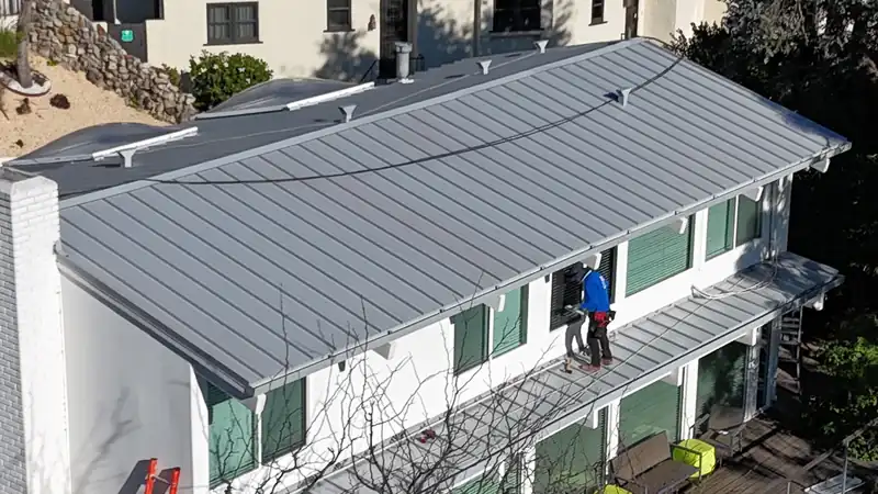 Installer working on a silver standing seam roof over a two-story white house