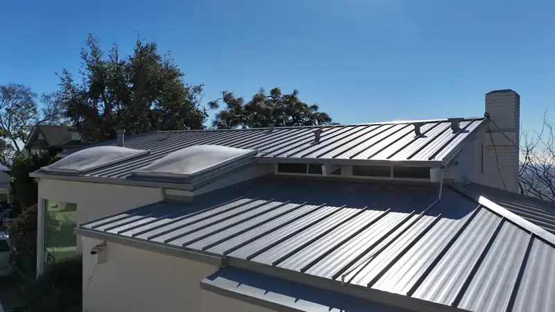 Silver standing seam metal roof with skylights and a long low-slope run, against a clear blue sky