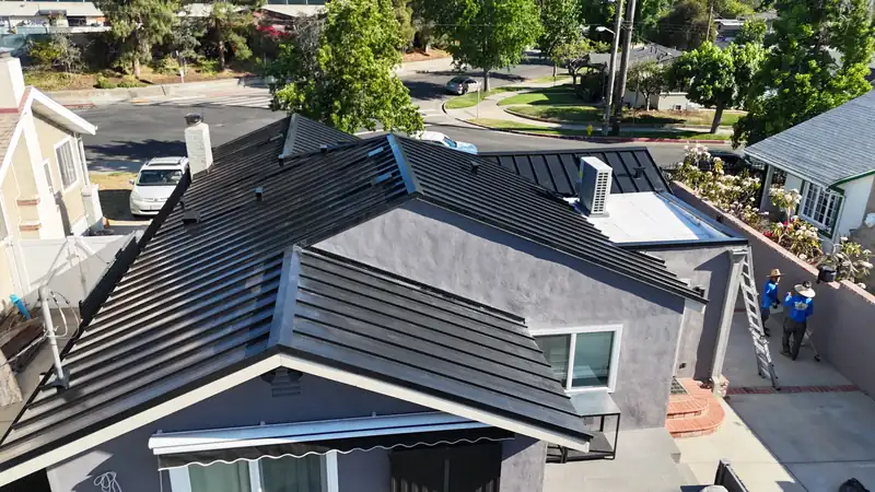 Black standing seam hip roof on a stucco house, with the crew finishing at the ladder