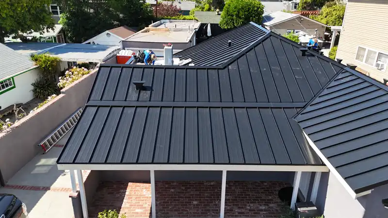 Black standing seam panels meeting at a hip and a valley over a covered patio