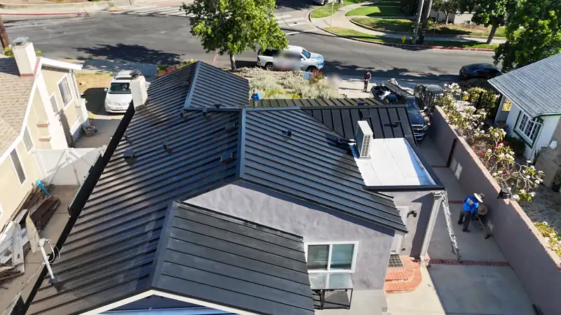 Crew finishing a black standing seam roof installation, with the ladder and materials staged below